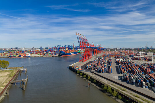 Aerial view of Waltershofer Hafen with red gantry cranes and rows of colorful shipping containers under a blue sky in Hamburg, Hamburg, Germany.