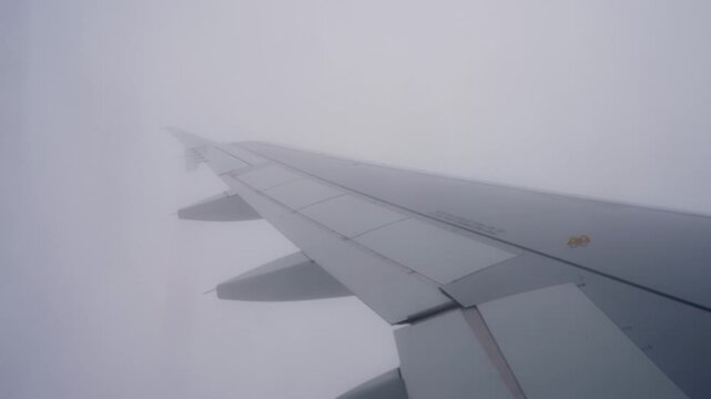 Airplane wing fades into near-white cloud during descent, capturing a full whiteout moment with minimal visibility and a quiet suspended in-flight atmosphere.