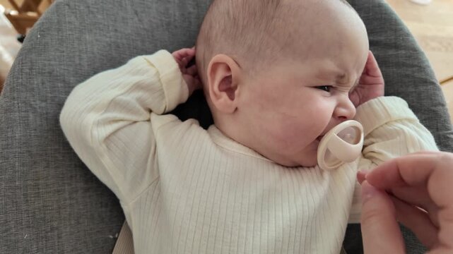 A parents hand gives a silicone pacifier to a small baby. The infant takes it into the mouth but spits it out a moment later. Close-up.