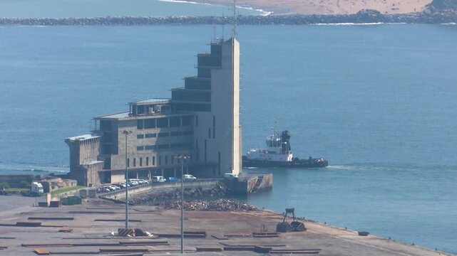 Tugboat navigates alongside modern concrete building at industrial port