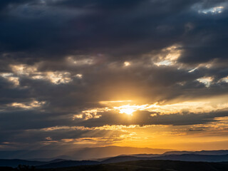 Obraz premium Sunlight breaking through dark storm clouds above mountain landscape