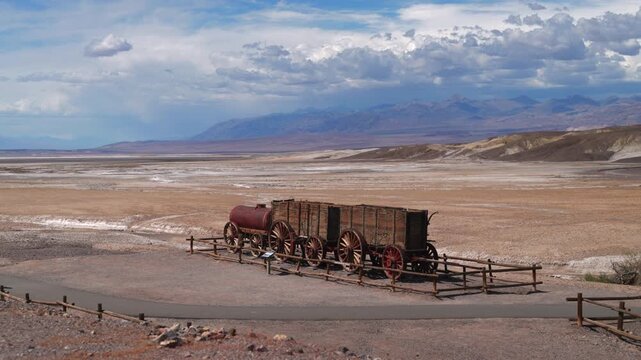 Vintage twenty mule team borax wagon display at Death Valley National Park with dramatic mountain backdrop and cloudy sky over vast desert landscape.