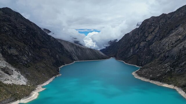 Huaraz, Peru: Forward footage of famous laguna paron in Caraz, Huaraz region, Peru. Surrounded by mountain range and with cloudy dramatic sky hiding cordillera blanca Piramide peak in the background