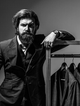 Suit. Male suits hanging in a row. Tailor in his workshop, designer. Bearded man in suit. Black and white