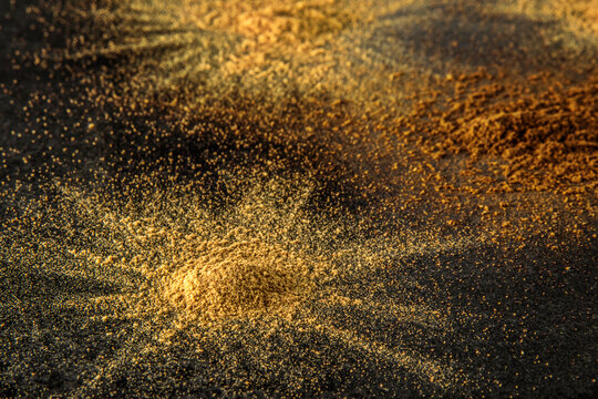 Ground spices creating abstract golden brown texture on dark background