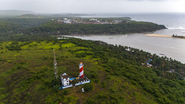 Aerial view of Betul Lighthouse with its red and white striped tower on lush green hills overlooking the river estuary and Arabian Sea in Kital, Goa, India.