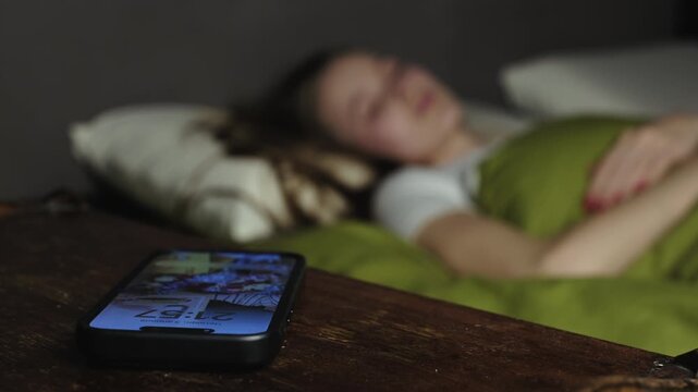Woman woken up by a phone call at night turning off the alarm and going back to sleep in her cozy bed in the bedroom