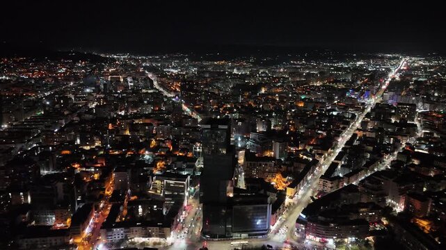 Aerial footage flying forward above downtown Tirana, Albania, showcasing illuminated city streets, architectural skyscrapers like TID Tower, and glowing grid lights at night