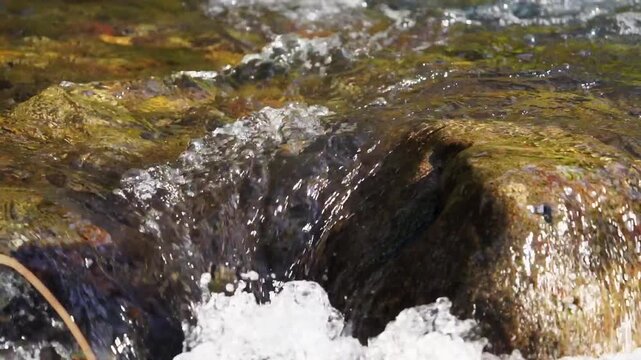 Real time close-up video of turbulent mountain river with crystal-clear water tumbling over small rapid of exposed rocks, boulders, with angle view of current directly above, nature footage, 120 fps
