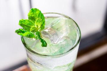 Cool mint leaf garnishes icy drink. Glass holds refreshing, sparkling beverage. Ice cubes float gently in clear liquid. Soft focus highlights vibrant green herb. Ideal for summer, relaxation © FatchurIsnandar