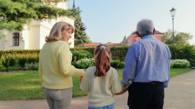 Older adult walks with child supportively. Older person guiding young child along trail nearby plants. An elderly individual and young child enjoy gentle walk together near floral garden