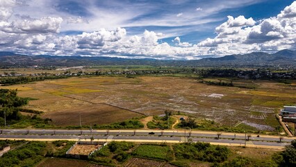 Aerial drone view of the vast golden rice fields surrounding Kontum City, Kon Tum Province, Vietnam's Central Highlands. The patchwork of rice paddies at harvest time stretches across the valley floor © jr