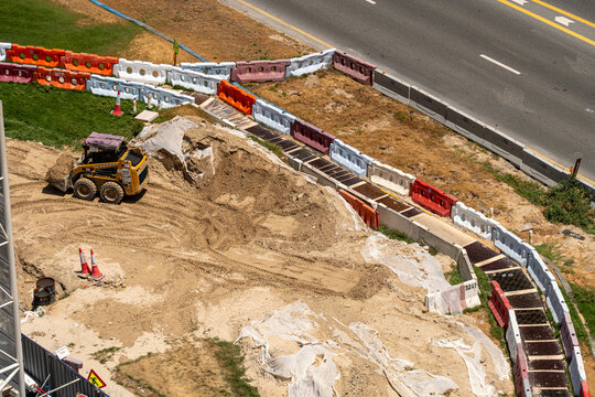 Aerial view of a yellow skid steer loader moving sand at a construction site bordered by colorful plastic barriers in Dubai, Dubai, United Arab Emirates.