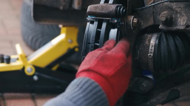 Driver installing new brake pad on passenger car during repair. Close up automotive maintenance with replacement friction pad mounted on brake caliper assembly. Vehicle brake system restoration and