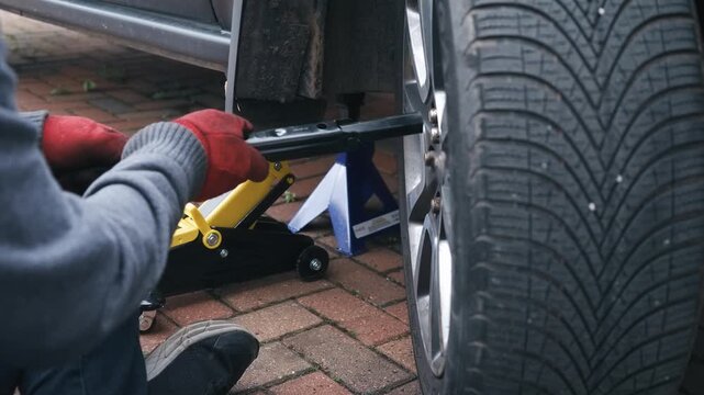 Lug wrench tightening wheel nuts during passenger car wheel installation. Gloved hands securing alloy rim fasteners after automotive brake maintenance and wheel mounting. Vehicle reassembly process