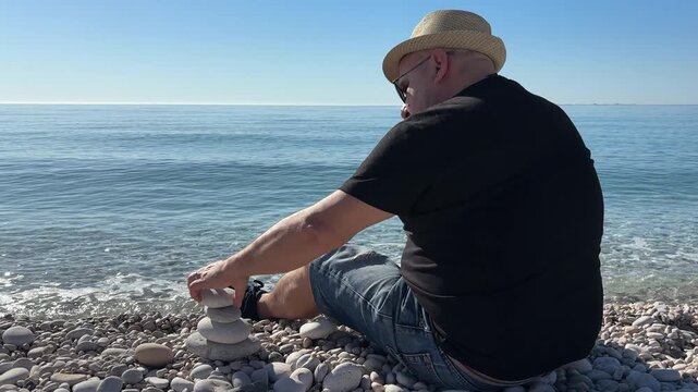 Hombre equilibrando piedras junto al mar en calma