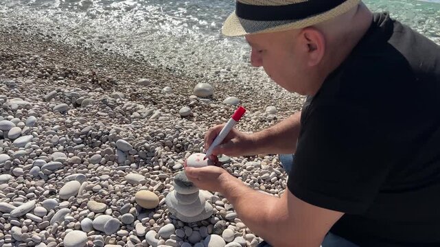 Hombre dibujando sonrisa en piedra junto al mar