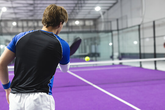 Man wearing sportswear holding racket preparing to hit yellow ball on purple court inside facility