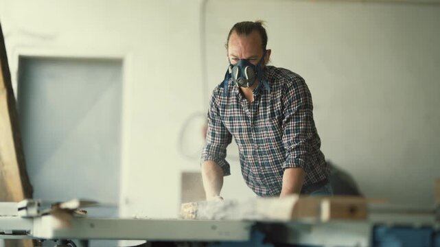 Carpenter with respirator mask sawing wood plank