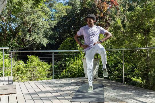 African American man balancing on exercise mat on wooden deck near metal railing wearing sportswear