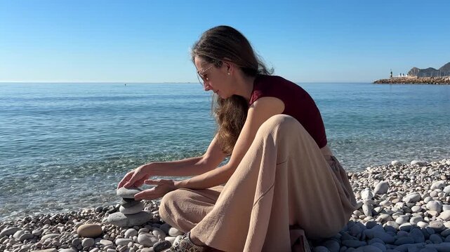 Mujer equilibrando piedras junto al mar en calma
