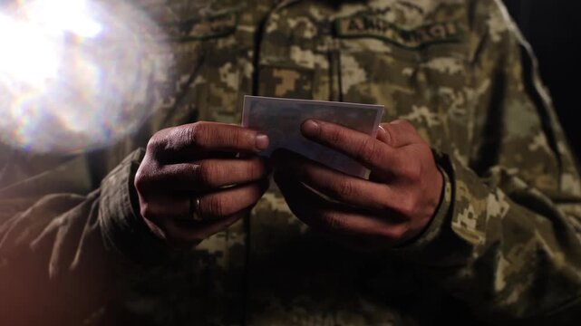 A cinematic close-up of a Ukrainian soldier in camouflage uniform holding a photograph of his family in his hands. This shot captures a deeply personal and emotional moment, emphasizing themes of long