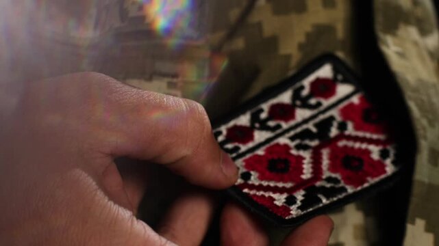 Close-up of soldier pulling traditional Ukrainian embroidered vyshyvanka patch from military uniform pocket. Strong symbol of national identity, cultural pride and wartime resilience