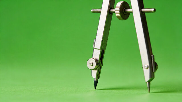 Close-up of a metal drafting compass on a green background, symbolizing education and precision.