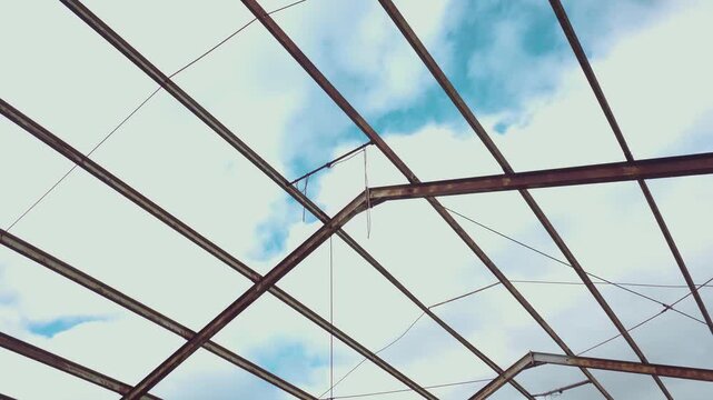 Hidden abandoned hangar roof with rusted steel beams and open sky above. Upward view revealing corroded metal framework wires and structural decay in secret military facility. Urban exploration mood