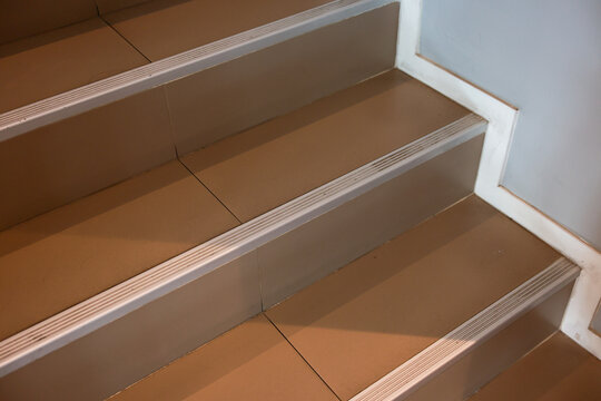 Close up view of indoor brown ceramic tile stair step with metal edge nosing for safety and slip protection in modern interior architecture providing calm and secure feeling for daily walking