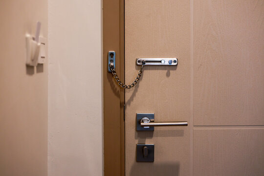 Close up of beige wooden door with heavy metal chain lock engaged for extra security and safety. Feeling secure inside private hotel room or home with handle and deadbolt locked tight