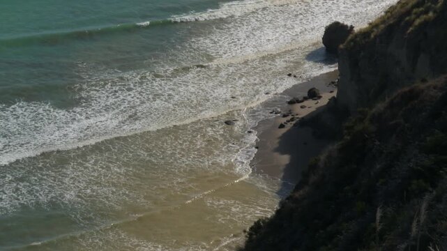 Waves washing onto narrow beach beneath steep coastal cliffs at Cape Kidnappers, New Zealand