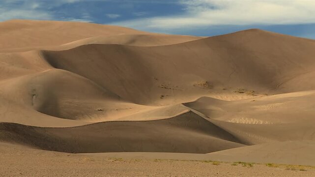 Smooth layered sand dunes with curved ridges beneath soft clouds in desert landscape at Great Sand Dunes National Park, Colorado, USA