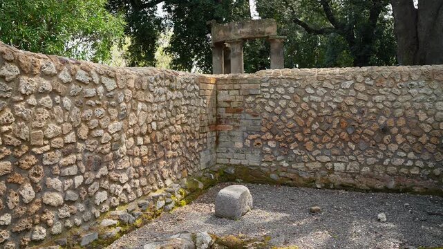 Sunlit stone courtyard in Pompeii with rough ancient walls, gravel floor, and a small shrine-like structure, capturing quiet Roman ruins without tourists.