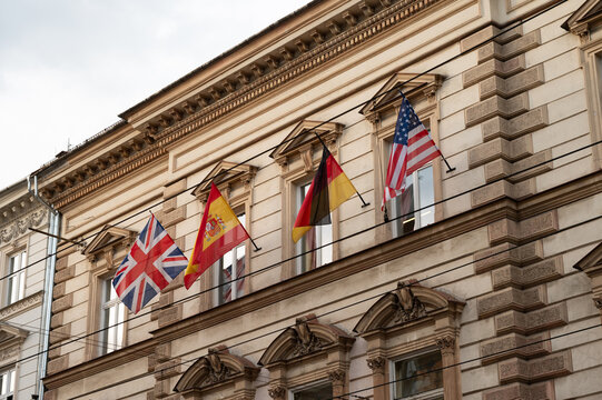 Low angle view of a historic European building facade decorated with international flags, including the UK, Spain, Germany, and the USA