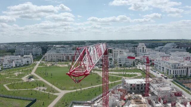 Drone shot moving from right to left past the jib of a tower crane above a large urban construction site in daylight.