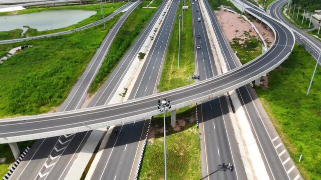 aerial view of modern highway interchange with multilayer roads and curved ramps surrounded by green farmland, showcasing transportation infrastructure, urban development, and road network planning.