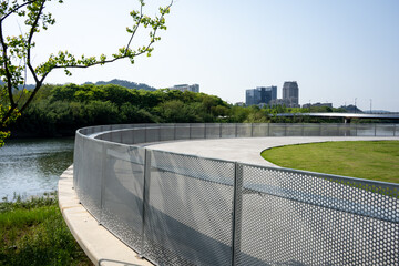 Fototapeta premium Curved metal fence surrounding green lawn and river in urban park landscape