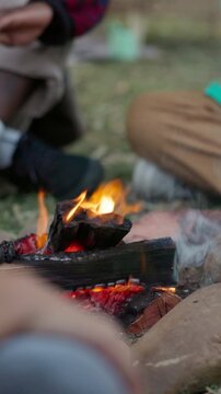Campfire, outdoor and travel in nature with friends, legs and bonding with group on weekend in woods. Holiday, adventure and warm with fire in forest, feet and hangout with people or social gathering