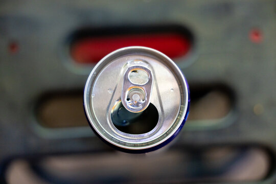 Top view macro photograph open aluminum beverage can showing metallic pull tab sitting against dark blurred background invoking refreshing satisfying feeling for thirsty consumer