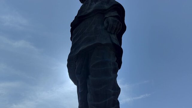 Low-angle tilt up revealing bronze sculptural texture and draped robe detail of Statue of Unity against moody blue sky. Ideal for art docs, heritage, and cinematic sequences.