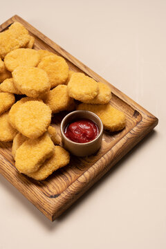 Chicken nuggets on wooden board over light beige background, crispy fast food snack concept