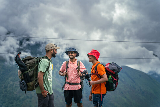 Three hikers with backpacks talking during a mountain trek at Ali Bedni Bugyal, Chamoli, Uttarakhand, India