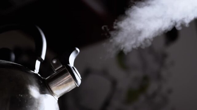 Close up, whistling metal kettle boiling on stove in kitchen. Retro kettle with rising steam in sunlight rays. Steam texture on blurred background. Vintage cozy atmosphere. Morning
