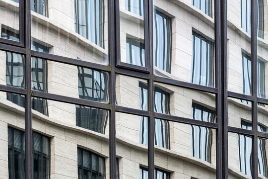 Urban architecture appears inside glass reflection on a corporate building facade, where abstract geometry and windows flatten depth into a calm grid