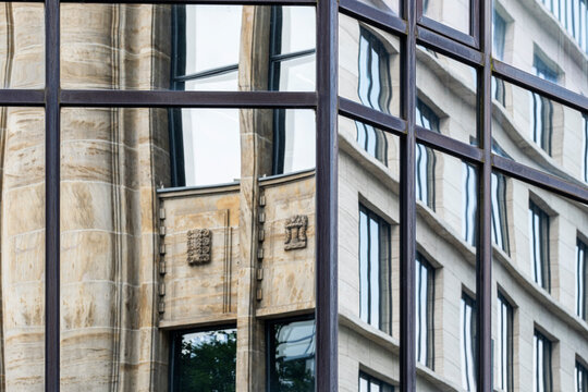 Glass reflection frames stone windows beside a corporate building facade, mixing urban architecture with abstract geometry and narrow vertical depth