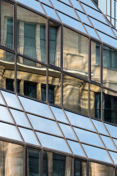 Glass windows bend a historic reflection across the corporate building facade, turning urban architecture into abstract geometry above stone detail