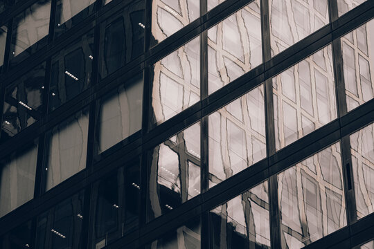Dark glass reflection divides the corporate building facade, where urban architecture turns windows into abstract geometry and shadowed diagonal depth