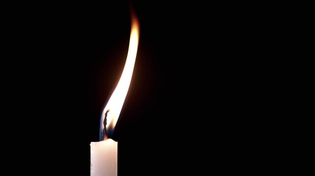 Side view, Isolated burning candle with bright flame on dark background. One white wax candle with calm yellow flame illuminates on black background. Copy space. Concept of memory,