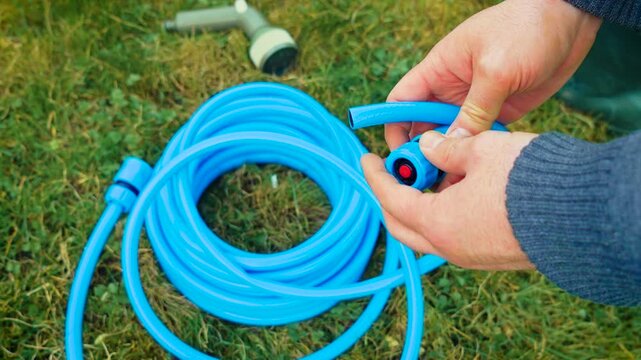 Securing quick connect fitting onto blue garden hose with hands on grass. Connecting hose coupling and assembling irrigation attachment for backyard watering setup. DIY lawn care preparation, outdoor